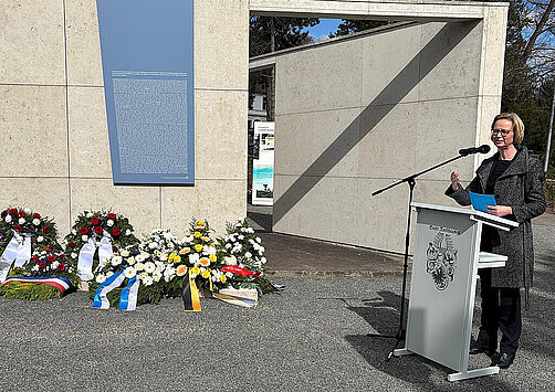 Thüringens Vize-Ministerpräsidentin und Finanzministerin Katja Wolf am Rednerpult, im Hintergrund sind viele Blumenkränze zu sehen
