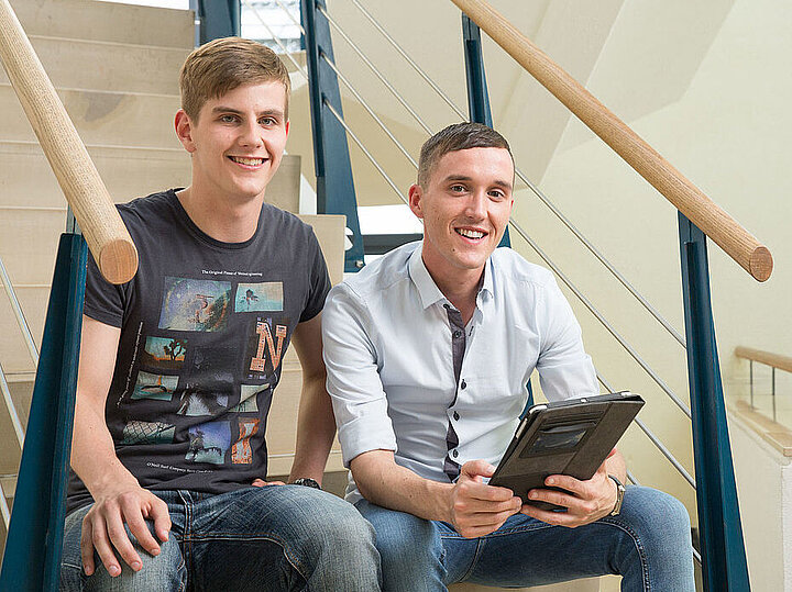 Zwei Studenten sitzen auf einer Treppe mit einem Tablet in der Hand.