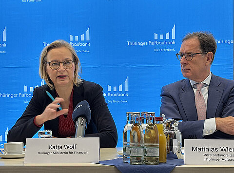 Finanzministerin Katja Wolf und Vorstandsvorsitzender der Thüringer Aufbaubank sitzen an einem Tisch mit Mikrofonen