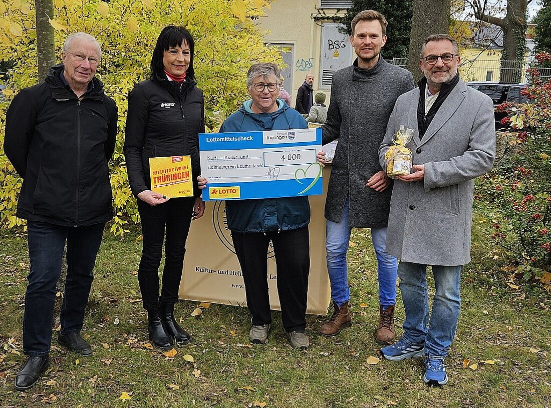 Finanzstaatssekretär Julian Vonarb mit einer Vertreterin von Lotto Thüringen und Vertreterinnen und Vertretern des KuHl e.V.. In der Hand hält er einen symbolischen Lottomittelscheck über 4.000 Euro.