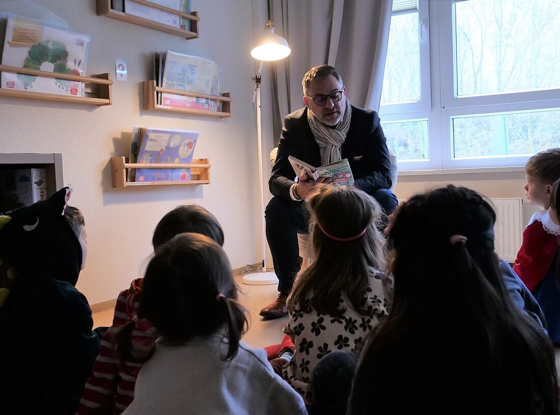 Finanzstaatssekretär Julian Vonarb sitzt vor einer Gruppe Kinder und liest ein Buch vor.