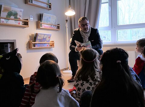 Finanzstaatssekretär Julian Vonarb sitzt vor einer Gruppe Kinder und liest ein Buch vor.