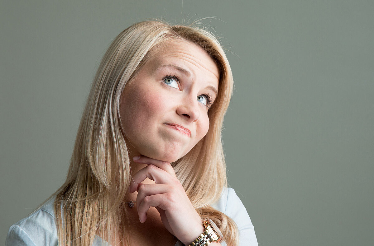 Junge blonde Frau schaut fragend nach oben.
