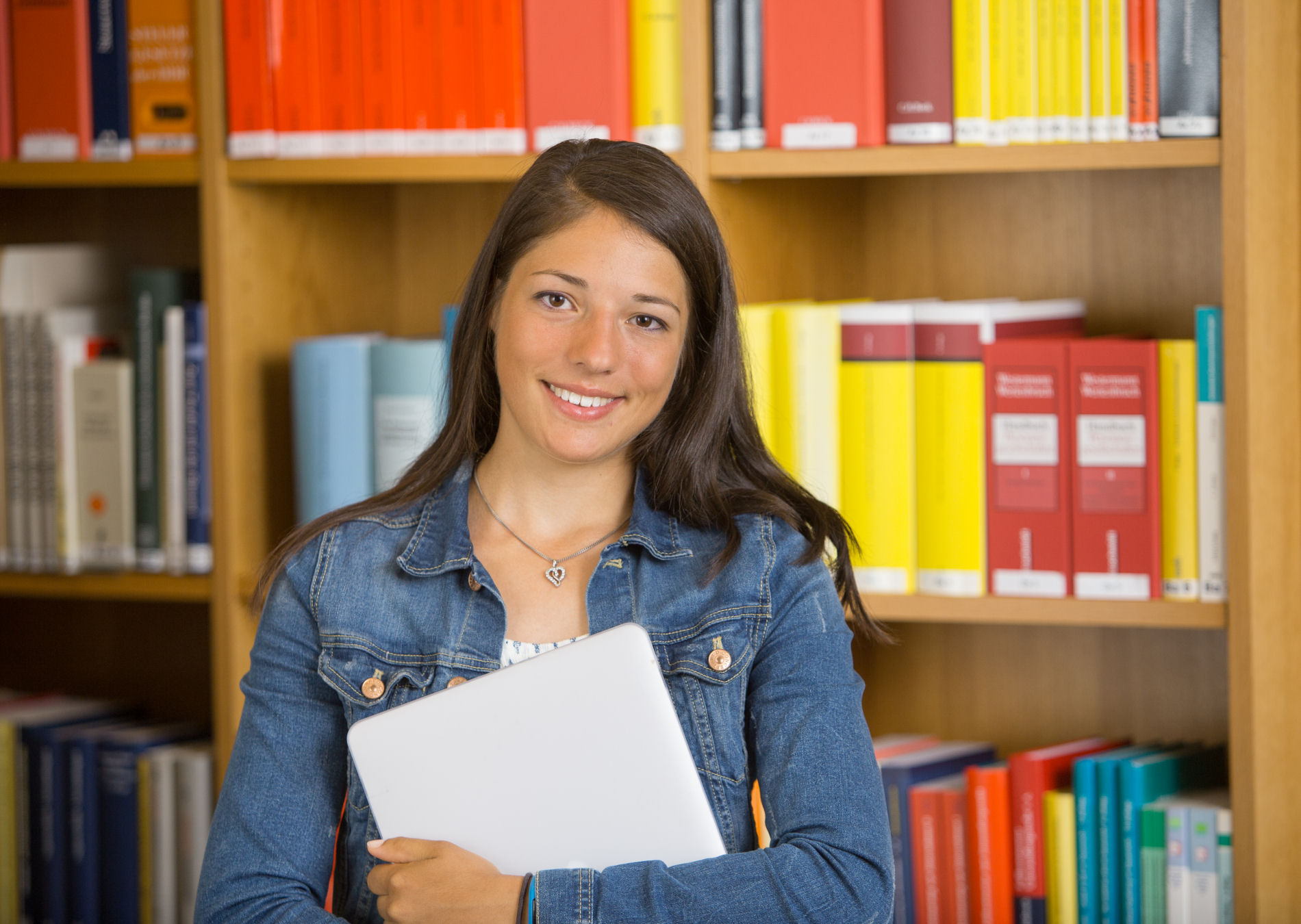 Laura steht vor einem Bücherregal und hat eine Mappe in der Hand